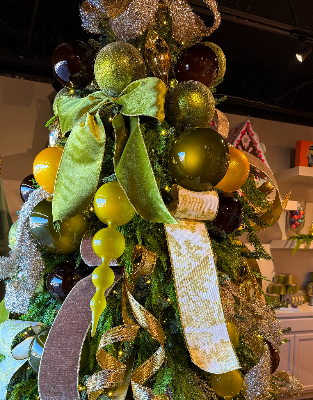Decorative Christmas tree topper with green and gold ornaments and ribbons at Mood by DMJ in Lafayette, LA.