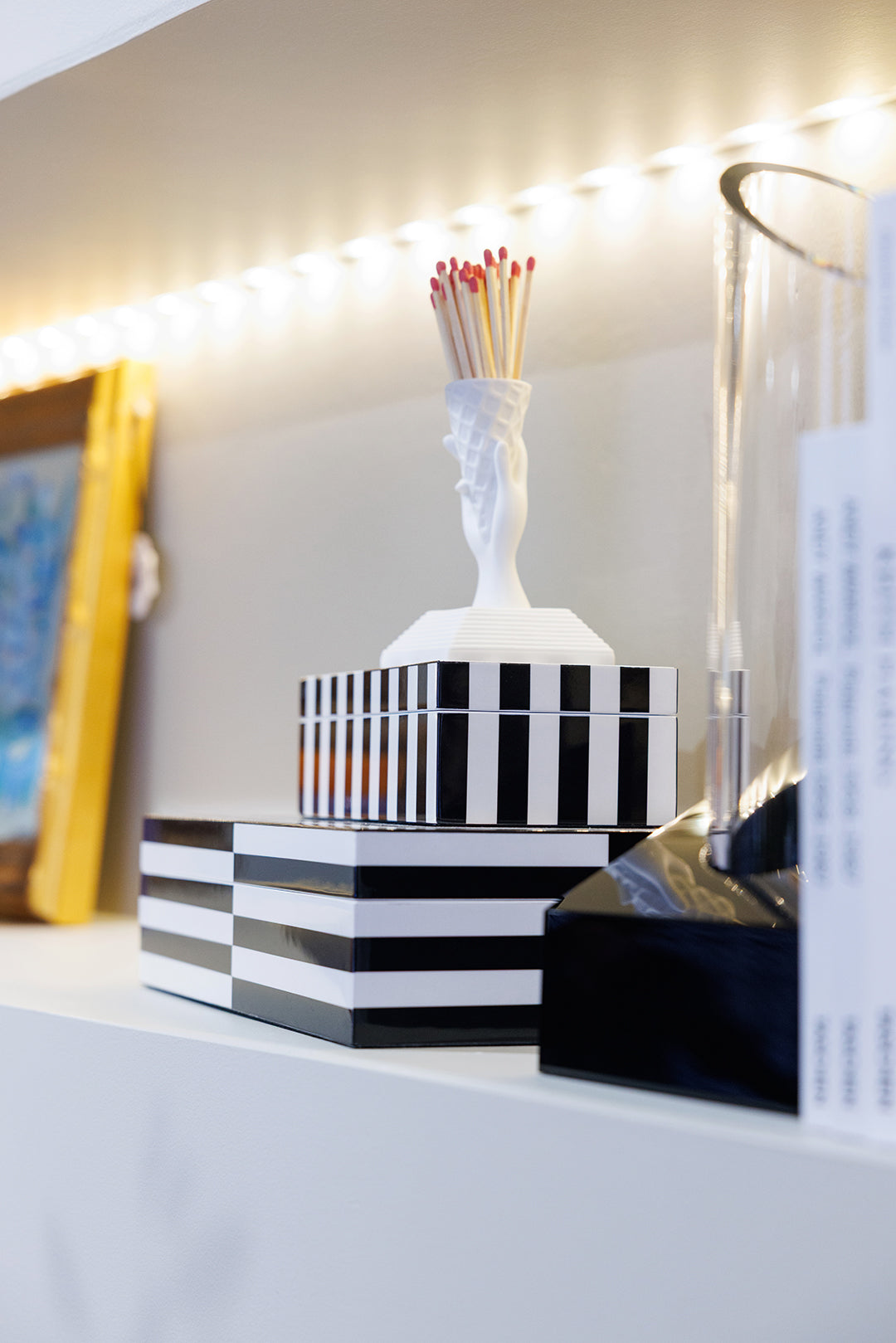 Black and white striped lacquer boxes and a white hand match holder displayed on a lit shelf at Mood by DMJ