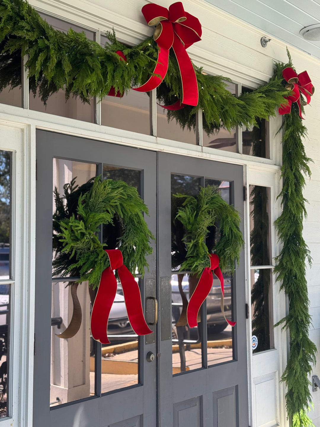 Holiday door decorated with fresh garland, Christmas wreaths, and red ribbon bows by Mood by DMJ in Lafayette, LA