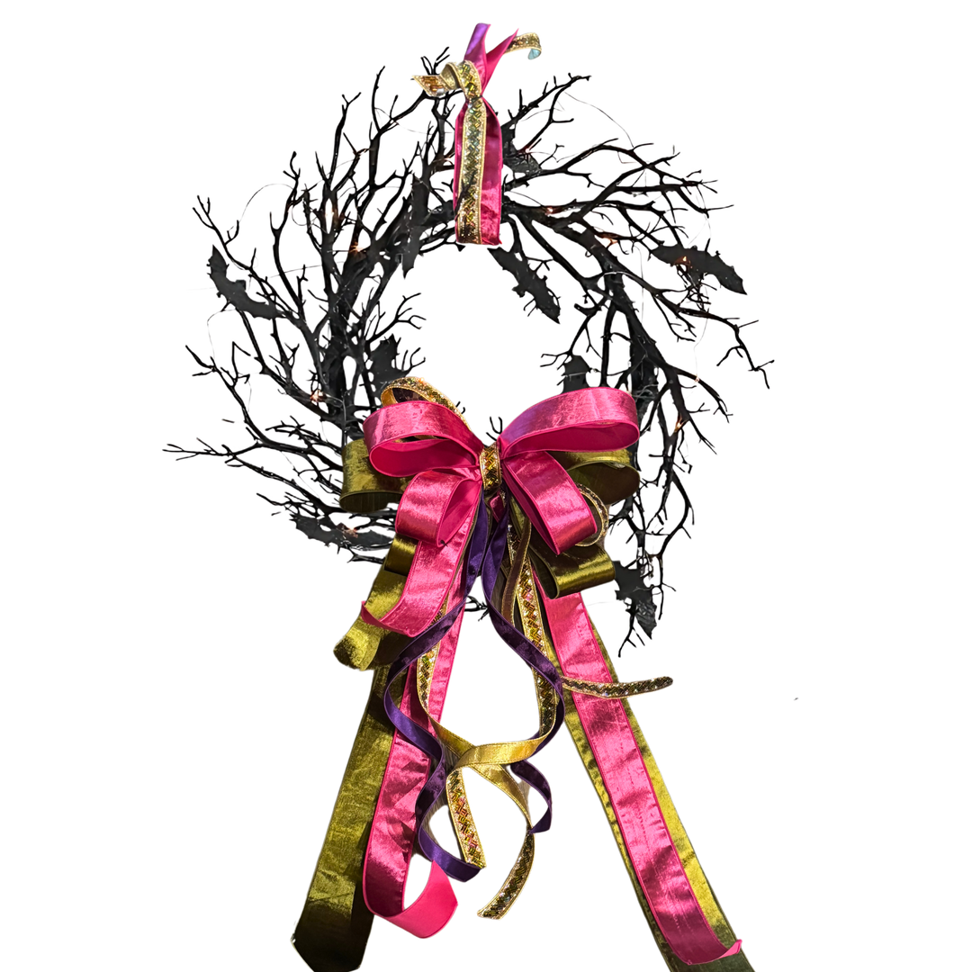 Decorative wreath with black branches and pink and gold ribbons on a white background Black Bat Wreath with Orange LED Lights for Halloween decor at Mood by DMJ in Lafayette, LA.