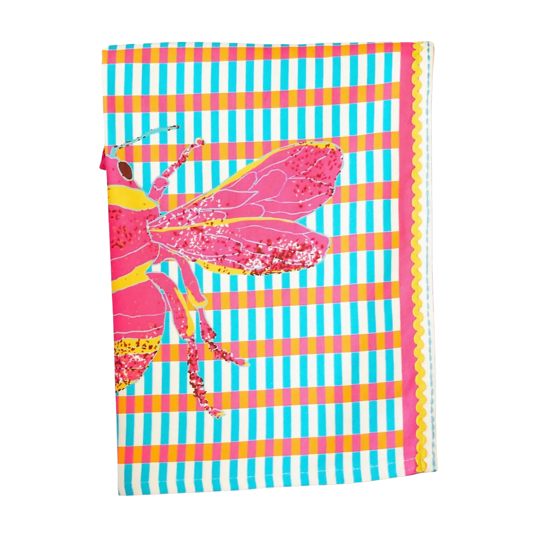 Pink BeeHaus kitchen towel with oversized graphic bees, pink check pattern, and zigzag trim displayed in a modern kitchen