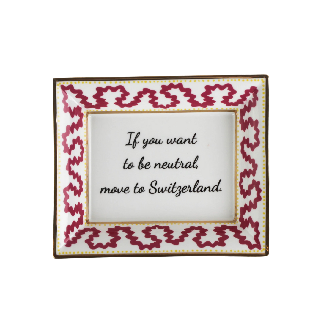 Pink porcelain trinket tray with gold edging and the phrase “If You Want to Be Neutral, Move to Switzerland,” styled as a decorative accent for Mood by DMJ.