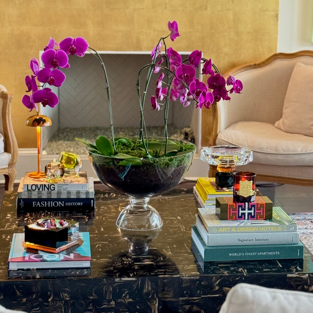 Decorative setup with purple orchids, books, and a bowl on a coffee table in a living room.