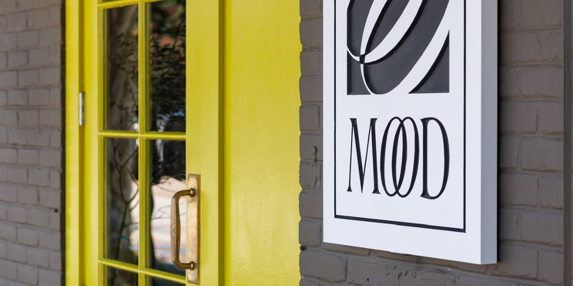 MOOD by DMJ storefront entrance with bright yellow door and modern black and white MOOD sign on brick wall, luxury home fragrance and lifestyle boutique in Lafayette Louisiana
