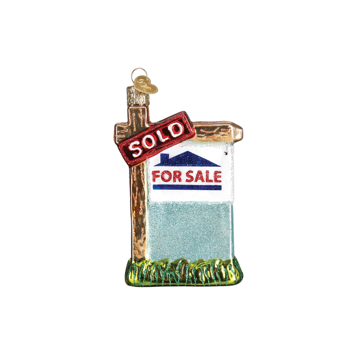 Realty Sign Ornament by Old World Christmas — red and white “SOLD” glass ornament hanging on a Christmas tree.