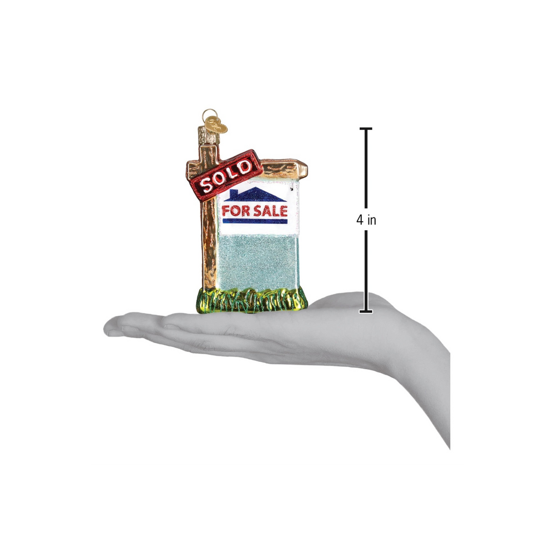 Realty Sign Ornament by Old World Christmas — red and white “SOLD” glass ornament hanging on a Christmas tree.