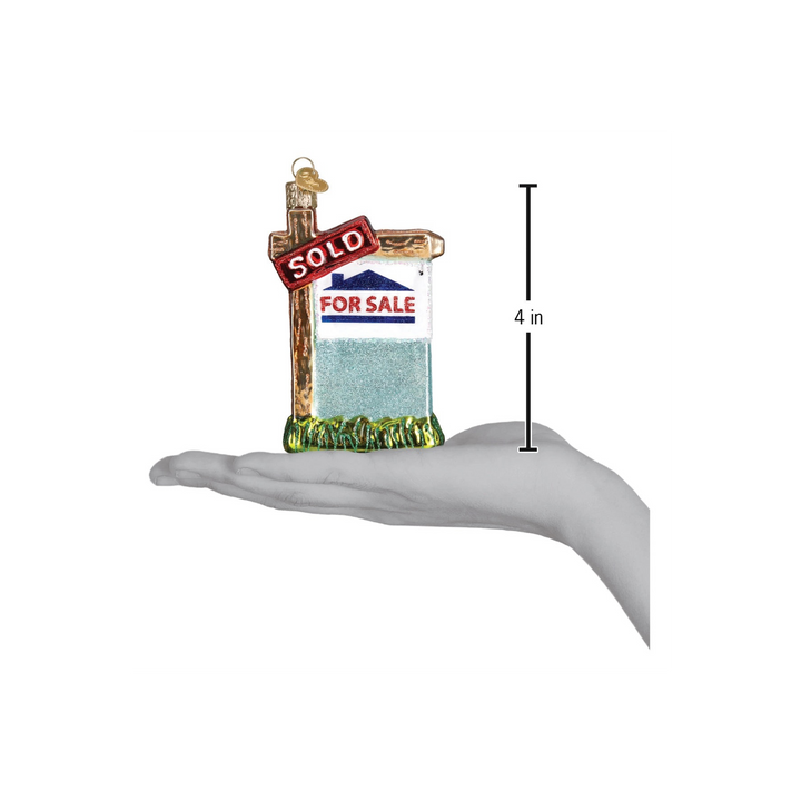 Realty Sign Ornament by Old World Christmas — red and white “SOLD” glass ornament hanging on a Christmas tree.