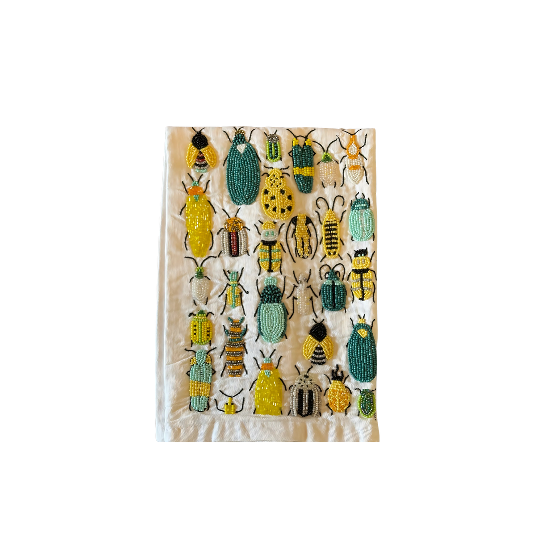 White cotton tea towel decorated with intricate beadwork in green, yellow, and black, featuring a collection of beetles in various sizes and patterns.