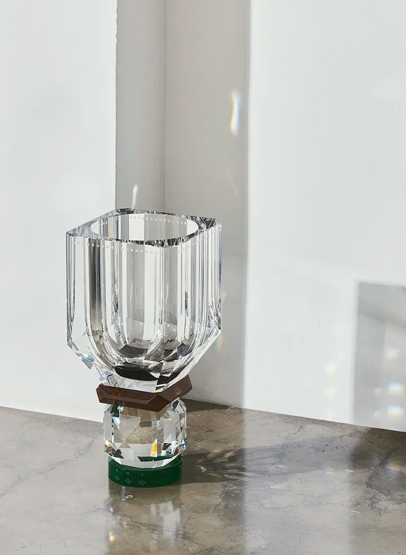 Utah Vase by Reflections Copenhagen in clear, brown, and green hand-cut crystal, displayed on a marble surface with sunlight reflecting through its faceted base.