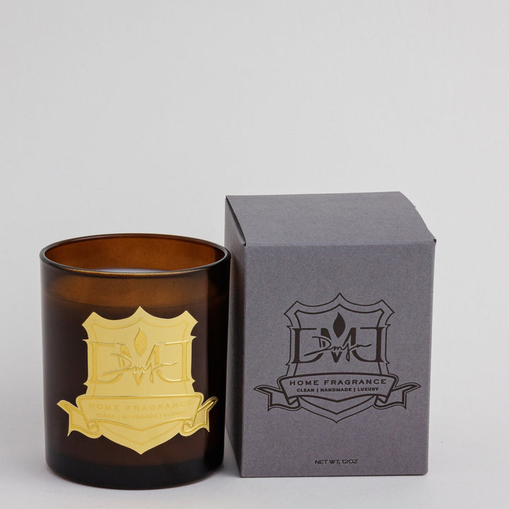 Lawn Affair Candle by DMJ Home Fragrance in dark amber glass with a gold crest label, beside its gray DMJ gift box, 12 oz
