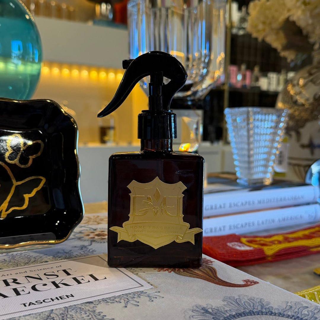 DMJ Home Fragrance Room &amp; Linen Spray in an amber glass bottle with a gold crest label, styled at Mood by DMJ in Lafayette