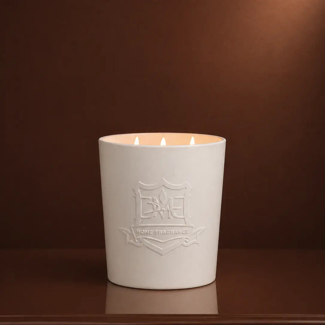 Lit DMJ Home Fragrance Big Boy 55 oz triple-wick coconut wax candle in a hand-cast white ceramic vessel with embossed DMJ crest
