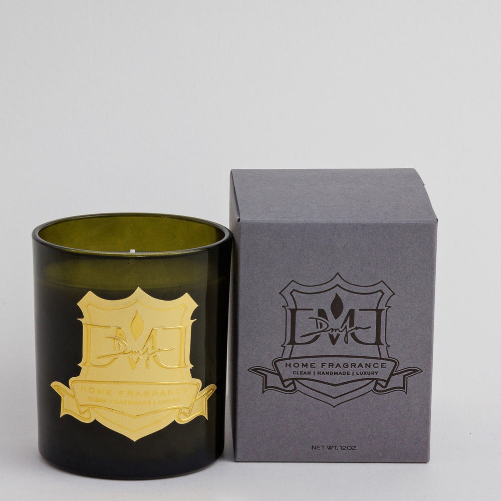 Woods Candle by DMJ Home Fragrance in olive green glass with a gold crest label, beside its gray DMJ gift box, 12 oz