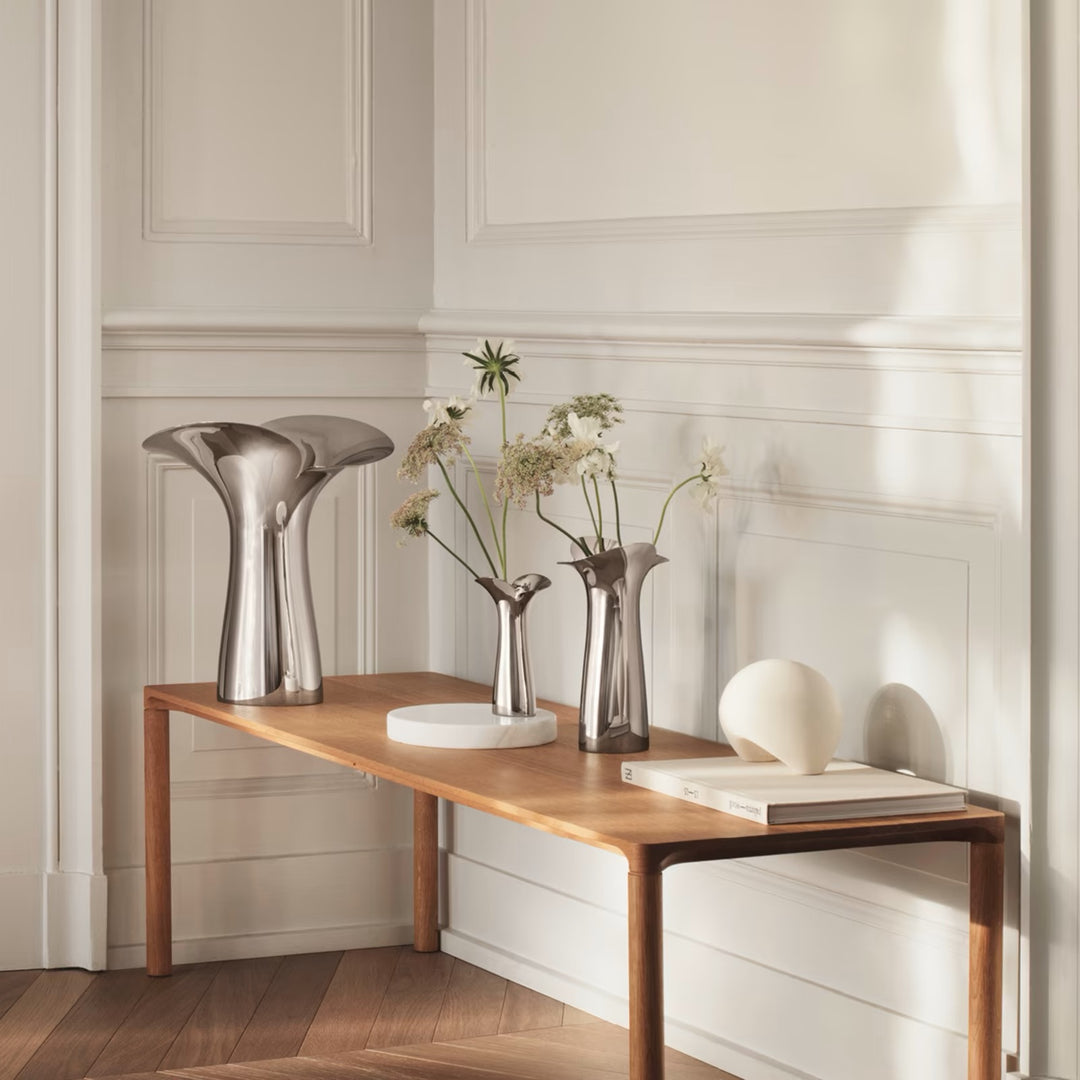 Georg Jensen Bloom Botanica stainless steel vases grouped with fresh stems on a wooden console table