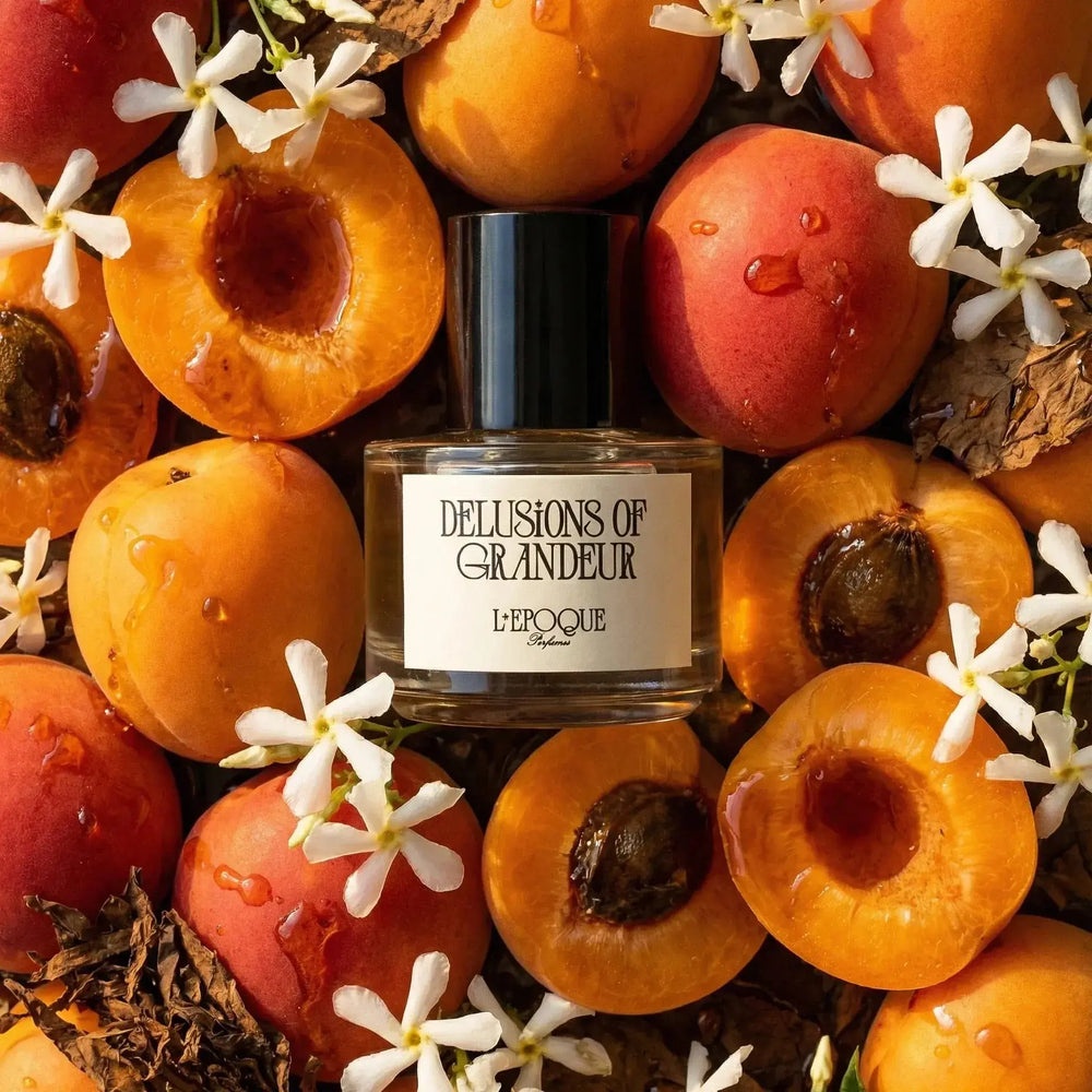 Delusions of Grandeur Eau de Parfum by L'Epoque Parfums surrounded by fresh apricots, jasmine sambac flowers, and spices representing its