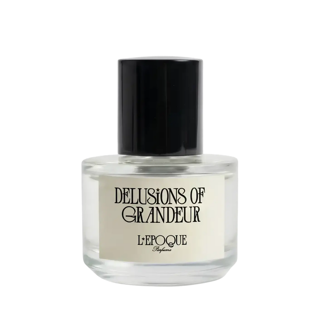 Clear glass bottle of Delusions of Grandeur Eau de Parfum by L'Epoque Parfums with black cap on a white background