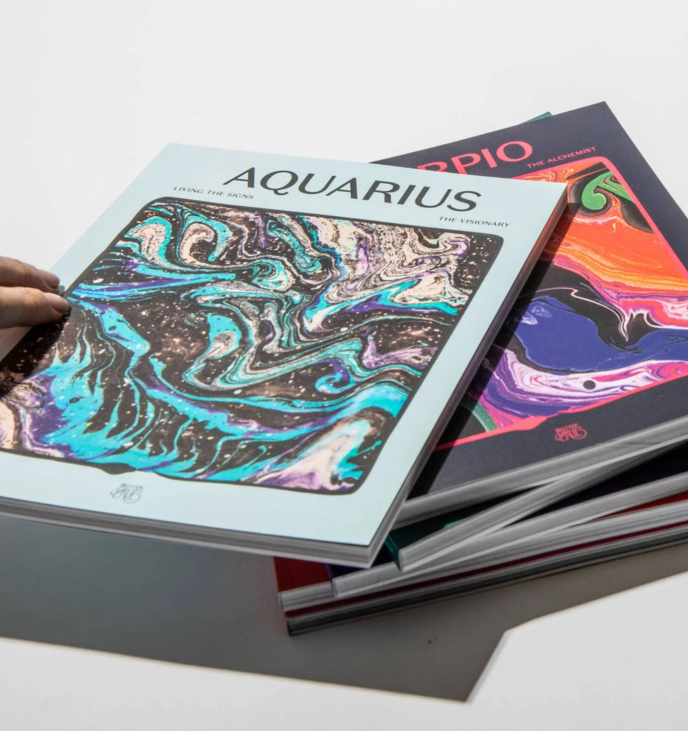 Hand holding Living the Signs: Aquarius, The Visionary above a stack of other In Case of Emergence zodiac workbooks