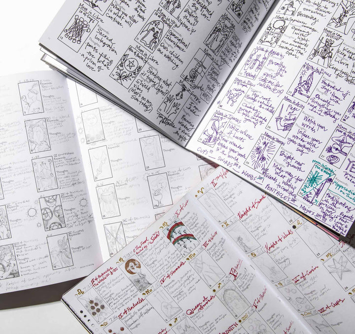 Open Living the Signs workbooks filled with handwritten tarot journaling and sketched card spreads