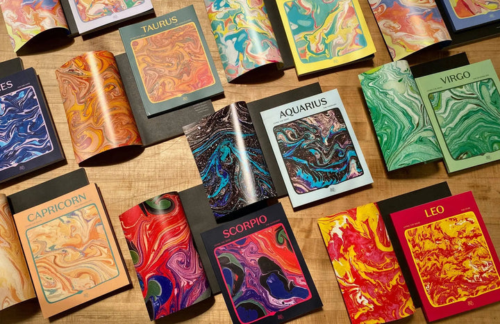 The full Living the Signs zodiac workbook series by Britten LaRue spread out on a wooden table, Leo in the corner