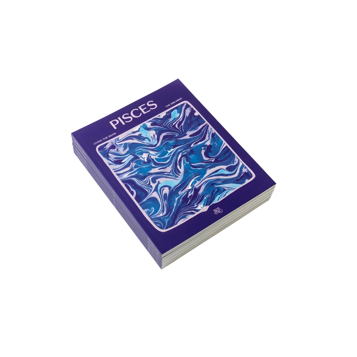 Living the Signs: Pisces astrology workbook by Britten LaRue, angled violet paperback with blue marbling on black