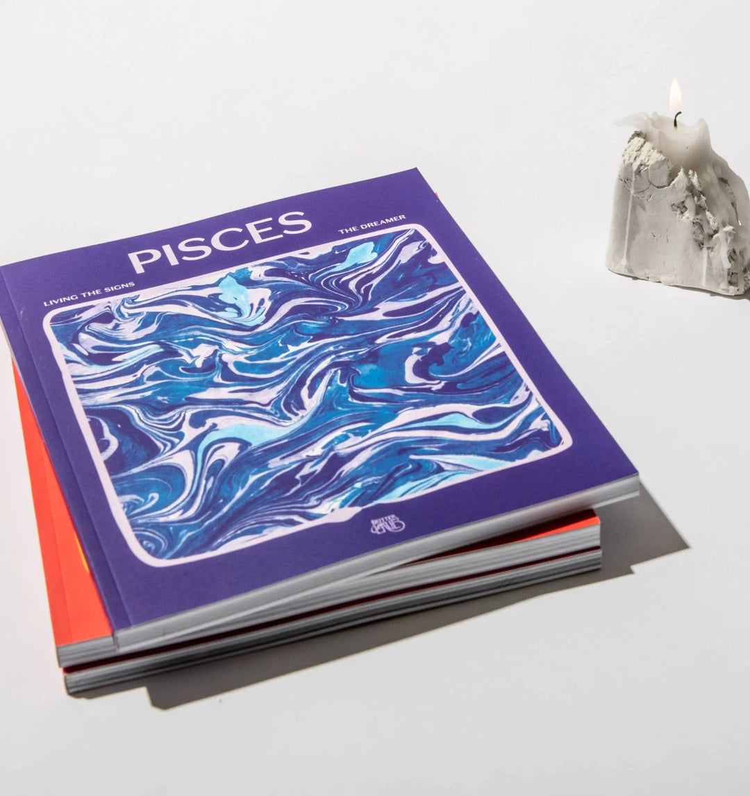 Living the Signs: Pisces workbook by Britten LaRue resting on a stack beside a melted white candle
