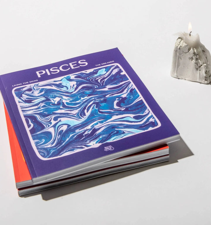 Living the Signs: Pisces workbook by Britten LaRue resting on a stack beside a melted white candle
