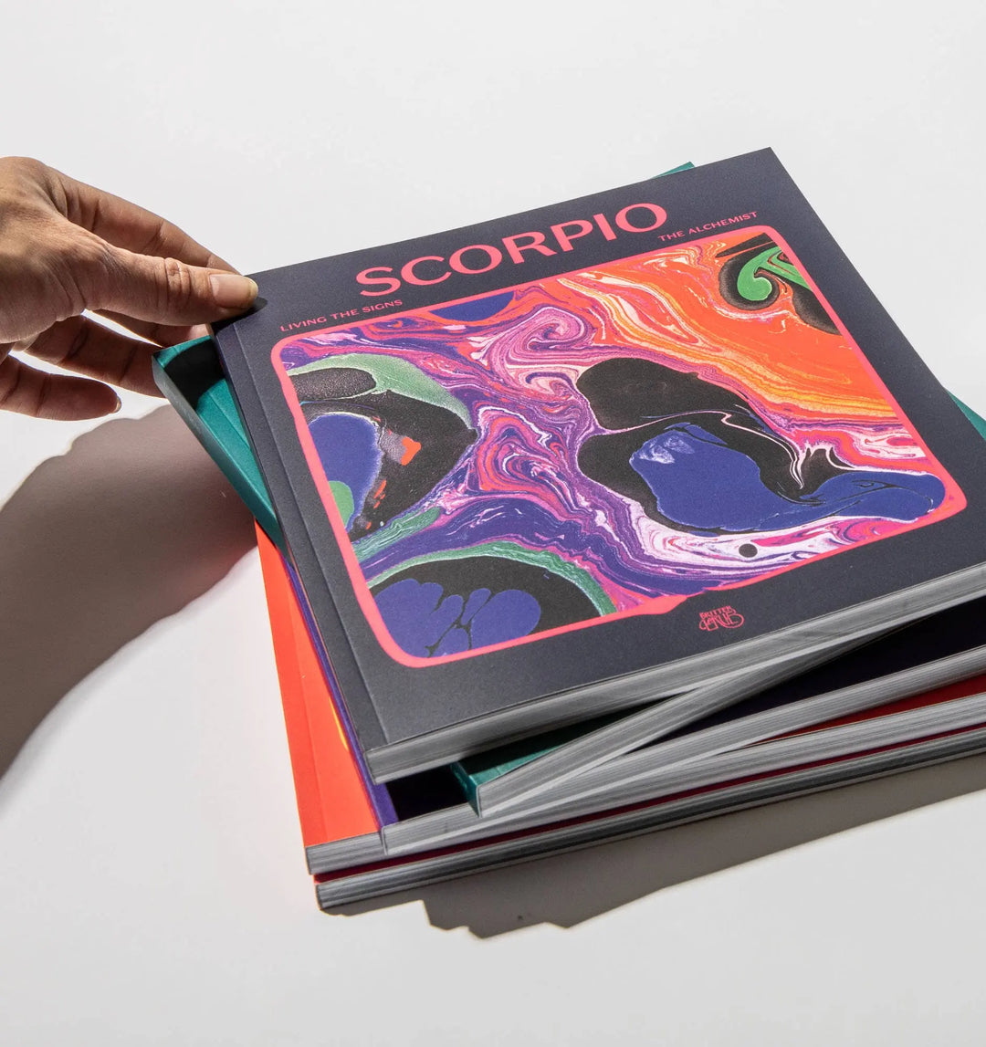 Hand lifting Living the Signs: Scorpio by Britten LaRue from a stack of zodiac workbooks