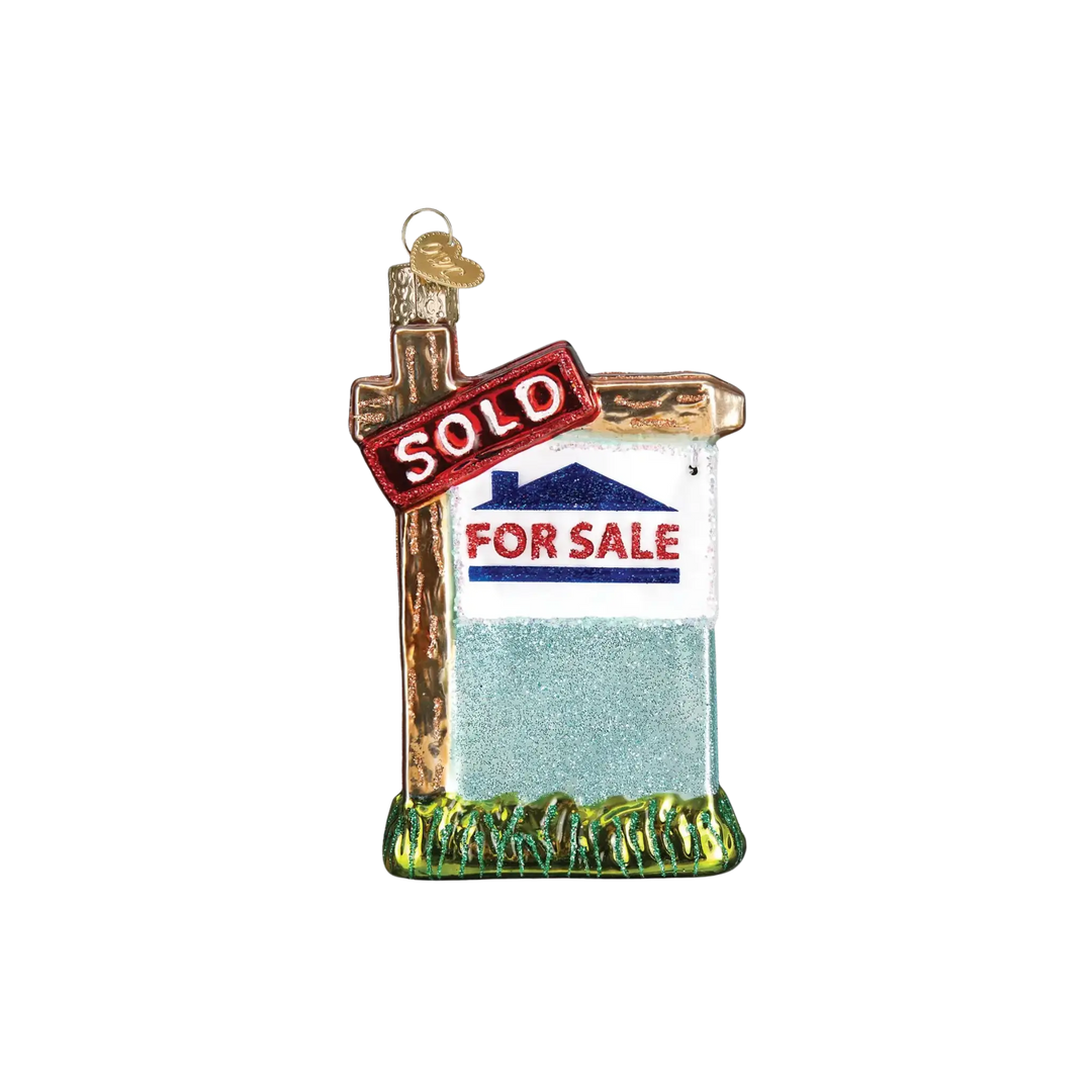 Realty Sign Ornament by Old World Christmas, red and white “SOLD” glass ornament hanging on a Christmas tree