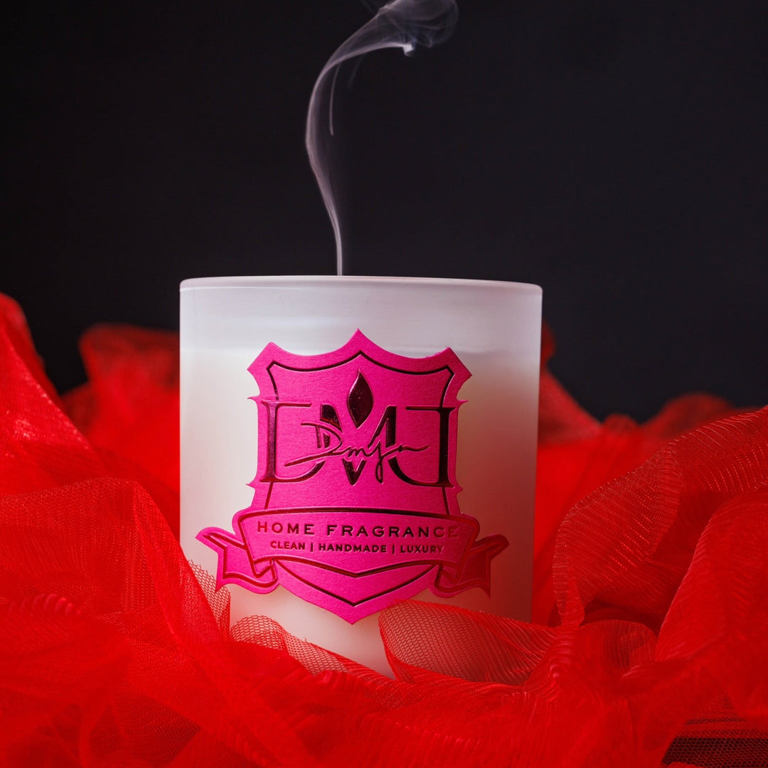 R'Oud luxury amber oud candle by DMJ Home Fragrance in white signature glass vessel with red rose petals — hand-poured coconut wax candle with bergamot, jasmine, rose, amber oud, and sandalwood, made in Lafayette, Louisiana.