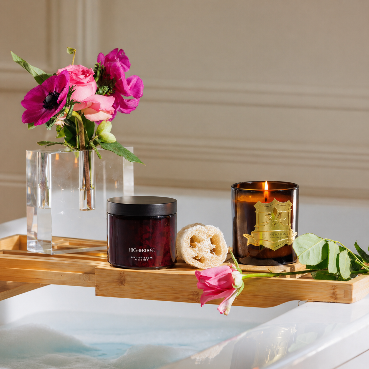 The Unwind Set with HigherDOSE Serotonin Soak and DMJ Pillow Talk Candle styled on a wooden bath tray with fresh pink flowers for a relaxing self-care gift